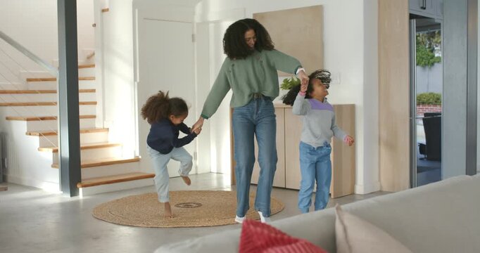 African American mother and two girls pulling hands, spinning on round woven rug at home bonding