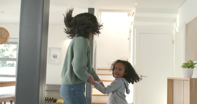 African American mother and daughter, child reaching up, hugging in greeting on round rug at entry