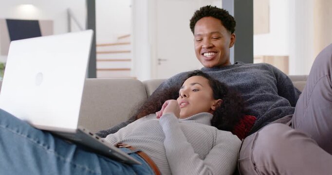 African American couple lounging on sofa at home, woman operating laptop reacting to funny clip