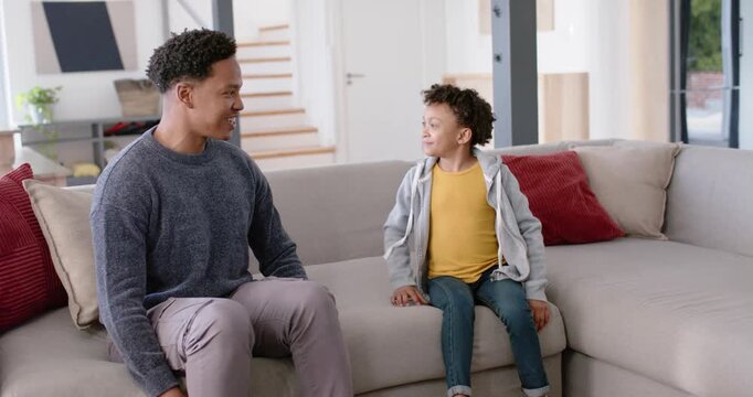 African American dad and school-aged daughter talking on sofa at home after dad prompt, gesturing