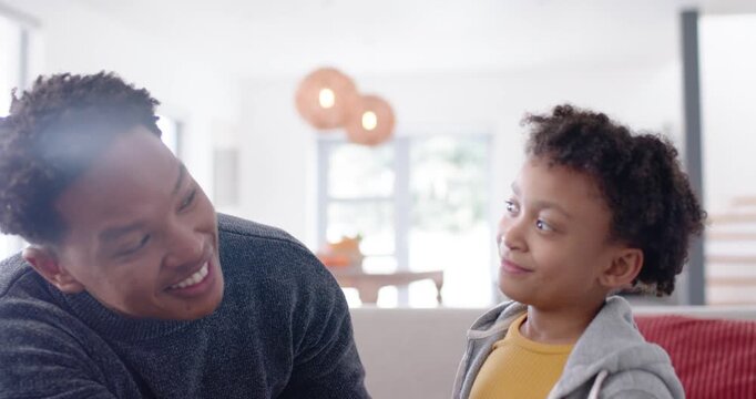 African American man and youth sitting on sofa at home, exchanging look, gesturing, entertaining