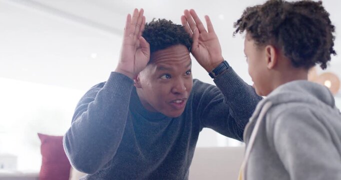African American father and son making antler gestures, son mirroring and high-fiving on couch