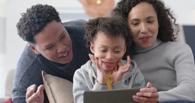 African American family leaning on sofa as child pressing cheeks tapping tablet, playing game