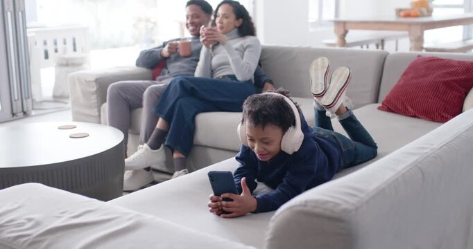 Family parents watching youth scrolling smartphone while lying on sofa wearing white headphones