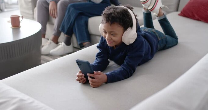 African American female child reacting to phone smiling and tapping on couch with white headphones