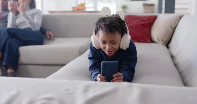 African American female youth lying on sofa headset holding phone laughing at phone