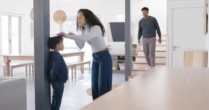 African American family measuring son's height at post at home using pencil notepad