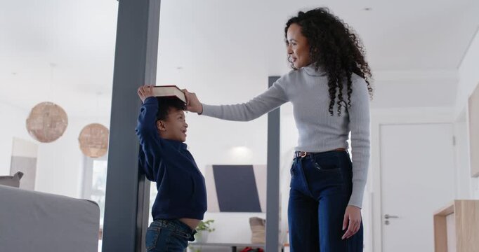 African American mother and son measuring height at home placing book at post noting growth