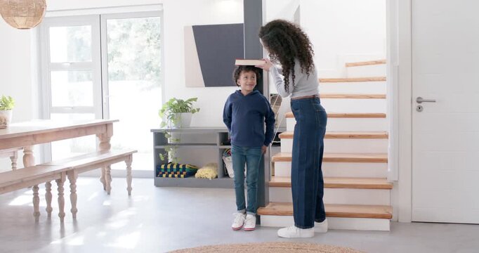 African American mother and child by post placing book on child's head at home, measuring height