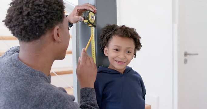 Anchoring tape on post, African American man measuring boy in hall, marking height with pencil