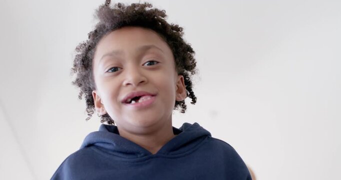 African girl child leaning over low camera, playing and smiling in navy hoodie under pendant light