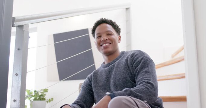 Camera zooming, African American man sitting on staircase straightening, smiling