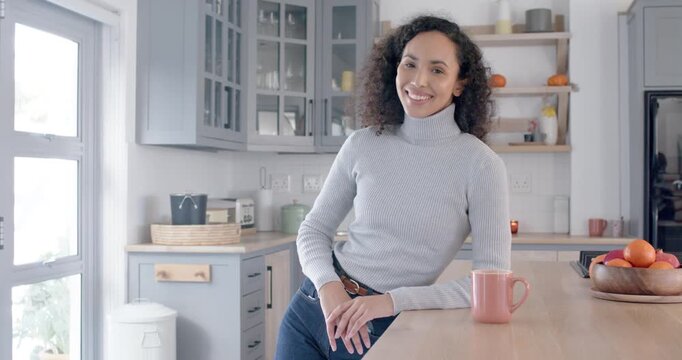 African American woman leaning on kitchen island, pink mug, smiling at camera during slow zoom