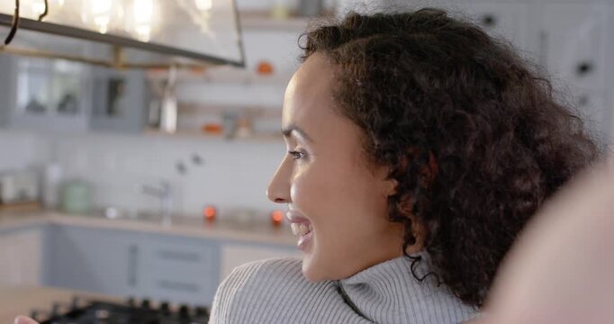 African American woman starting selfie, smiling, waving, chatting on phone in kitchen in gray top