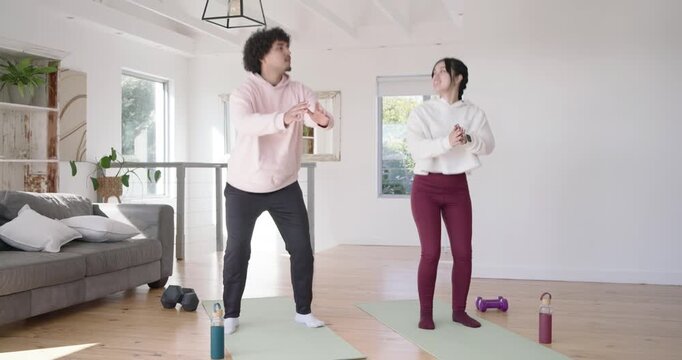 Diverse couple making eye contact and smiling, doing repeated squats on yoga mats for home workout