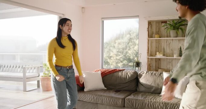 Asian woman and African American man smiling, mimicking, closing gap by gray couch preparing to hug