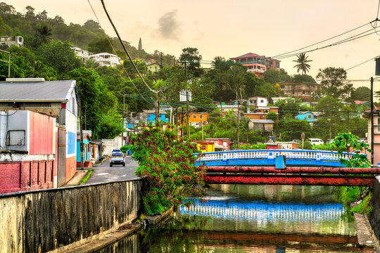 Colorful street and bridge over a canal with vibrant tropical houses on the hillside at sunset in Castries, Saint Lucia.