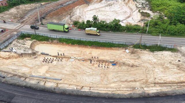 Aerial drone orbiting shot of an underpass construction site excavation with foundation piles and active highway traffic in a developing landscape.