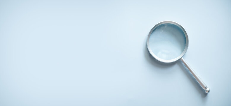 Silver magnifying glass on light blue background with copy space, concept of research, search, analysis, investigation, discovery, and minimalist business design.