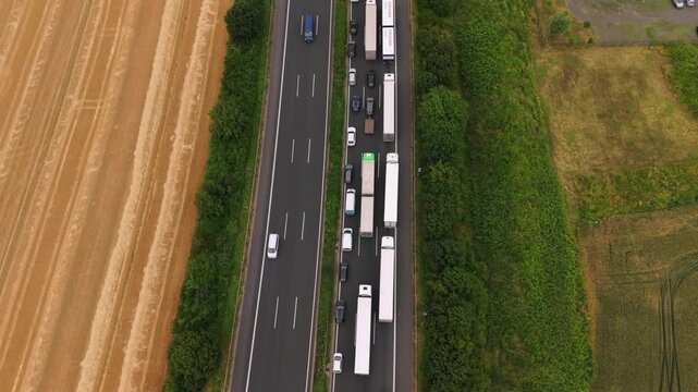 Aerial perspective of a congested highway filled with various vehicles, bordered by fields and industrial structures, highlighting traffic dynamics and landscape