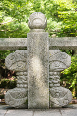 A carved granite bridge railing post topped with a lotus flower bud finial stands at a traditional Korean temple entrance. © 완수 안
