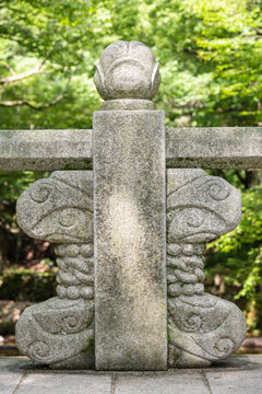 A carved granite bridge railing post topped with a lotus flower bud finial stands at a traditional Korean temple entrance.