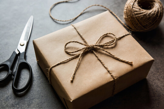 Brown paper package tied with twine beside scissors and a twine ball, minimalist craft