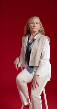 Vertical video: Mature woman sitting on stool during studio shoot with navy tie