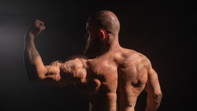 A male bodybuilder poses in shorts, showing off his back muscles.