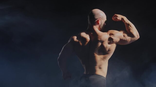 A male bodybuilder poses in shorts, showing off his muscles. 