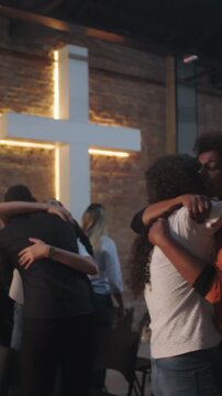 Devout multiethnic parishioners warmly embracing and comforting each other in front of an illuminated cross conveying holy love, sacred fellowship, and emotional healing
