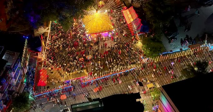 Kathmandu, Nepal, aerial shot of fast-moving street traffic and bustling crowds of devotees around the golden illuminated Maitidevi Temple during the Tihar festival of lights.