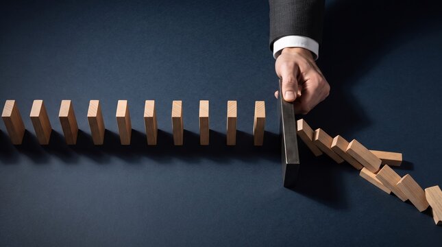 A businessman's hand intervenes to stop a line of falling dominoes, symbolizing risk management and crisis intervention.