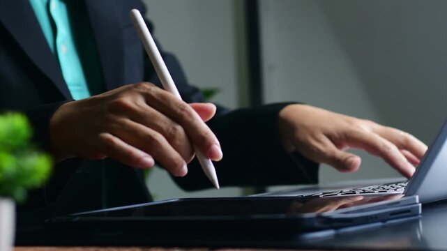 multitasking professional workspace concept showing businesswoman analyzing online reports on laptop and signing electronic documents with digital stylus on tablet in modern office.