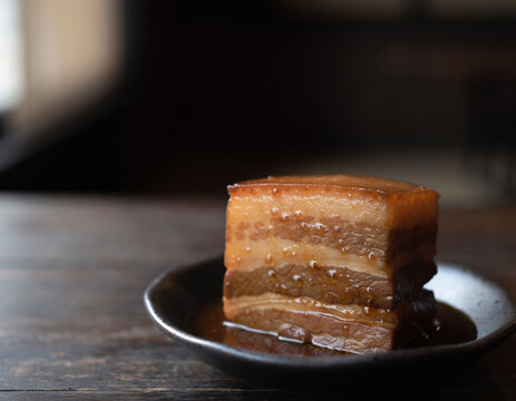 Close-up of Japanese buta no kakuni braised pork belly with glossy soy glaze in a dark ceramic bowl, tender layered meat, moody washoku still life