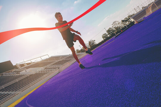 Silhouette of young man running sprinting to red finish line at the racetrack with speed zoom blur effect.. Finisher, marathon runner sprinting moment at the racetrack.