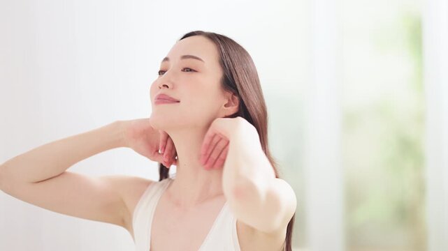 明るい部屋の中でヘアケアをする日本人女性(髪をかきあげる仕草)