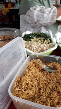 Close-up video of a food vendor's hands carefully wrapping nasi pecel, a traditional Indonesian rice dish served with mixed vegetables and savory peanut sauce, for a customer. Authentic local street f
