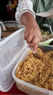 Close-up video of a food vendor's hands carefully wrapping nasi pecel, a traditional Indonesian rice dish served with mixed vegetables and savory peanut sauce, for a customer. Authentic local street f