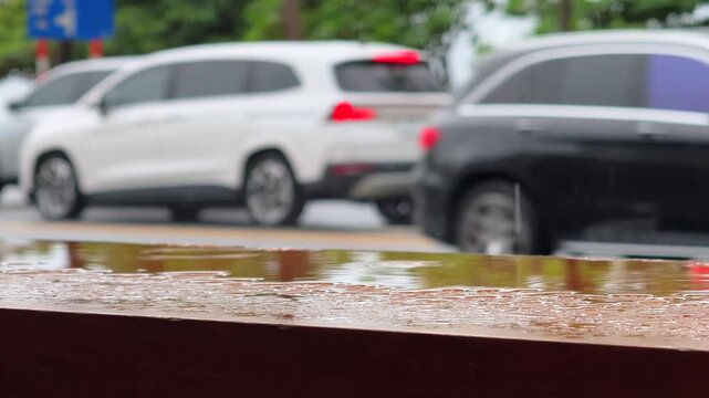 Close up of Wet outdoor table Surface under rain and Blurred Cars and Motorbike on the Street in the background