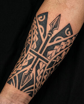 Traditional Polynesian inspired tribal blackwork tattoo with spear motifs wrapped around a man's forearm