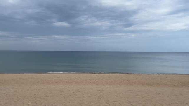 A quiet stretch of Tuy Hoa Beach in Phu Yen, Vietnam, with golden sand, gentle waves and a flat sea horizon beneath layered gray clouds.