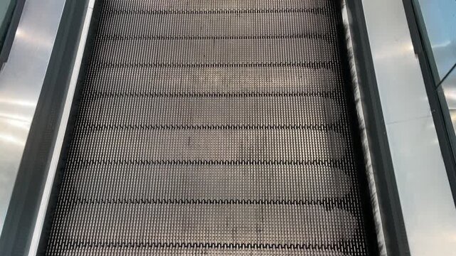 Close view of a supermarket travelator in Vietnam, showing repeating metal grooves, dark rubber handrails and glass sides forming parallel lines through the frame.