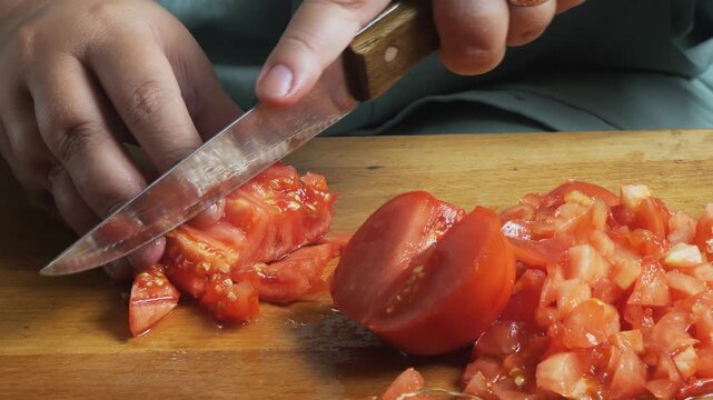 Slicing fresh red tomatoes with a knife on a cutting board on a wooden table