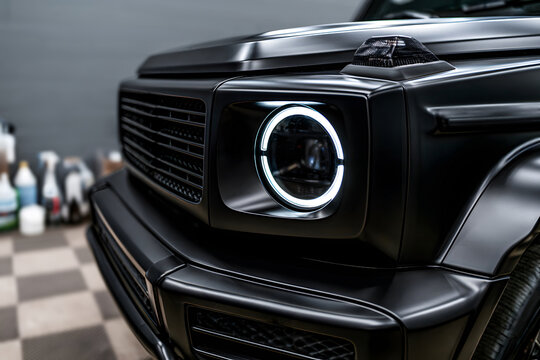 close-up of a matte black luxury suv round led headlight and front grille in a detailing shop, showcasing premium automotive design, custom tuning, and off-road power.