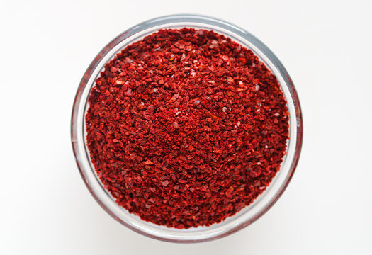 Top-down view of a clear glass bowl filled with coarsely ground red chili pepper flakes (gochugaru), isolated on a white background.