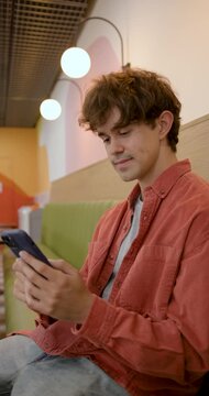 Young Man Using Smartphone in Cafe, Smiling