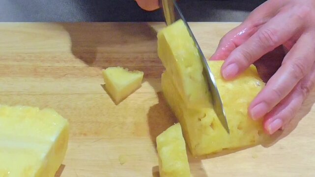 Hands Slicing Fresh Pineapple Lengthwise on Wooden Board