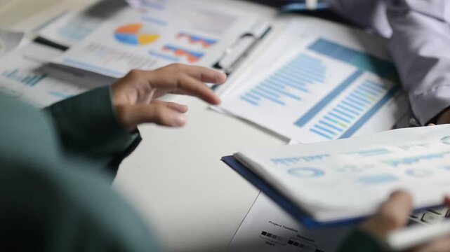 Close up of two asian colleagues working together, have a disussion and using laptop computer at office with financial document on desk