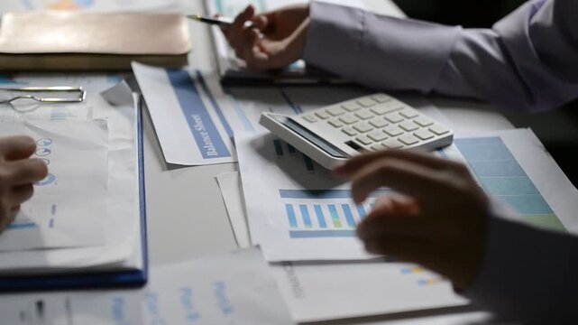 Close up of two asian colleagues working together, have a disussion and using laptop computer at office with financial document on desk